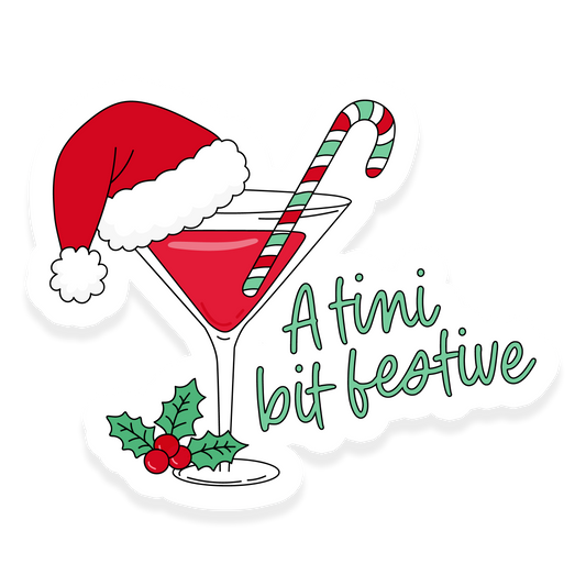 A festive martini glass sticker with a red drink, candy cane, and Santa hat, featuring holly leaves and the phrase “A tini bit festive.”